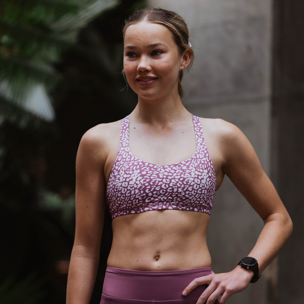 Woman wearing a purple sports bra and leggings with a blurred background