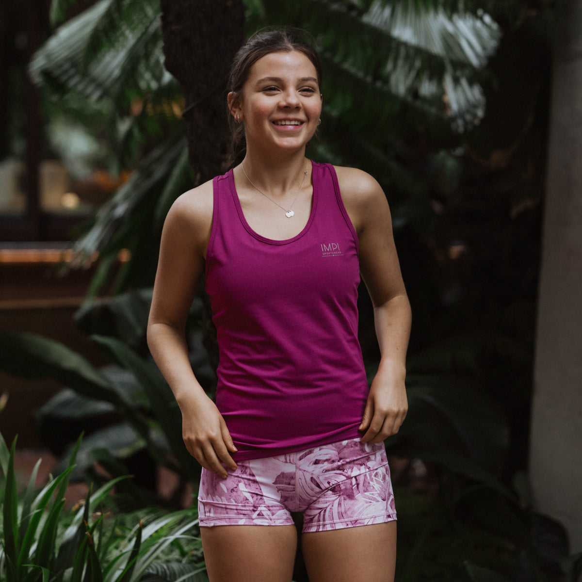 Woman wearing a purple tank top and patterned shorts standing among plants