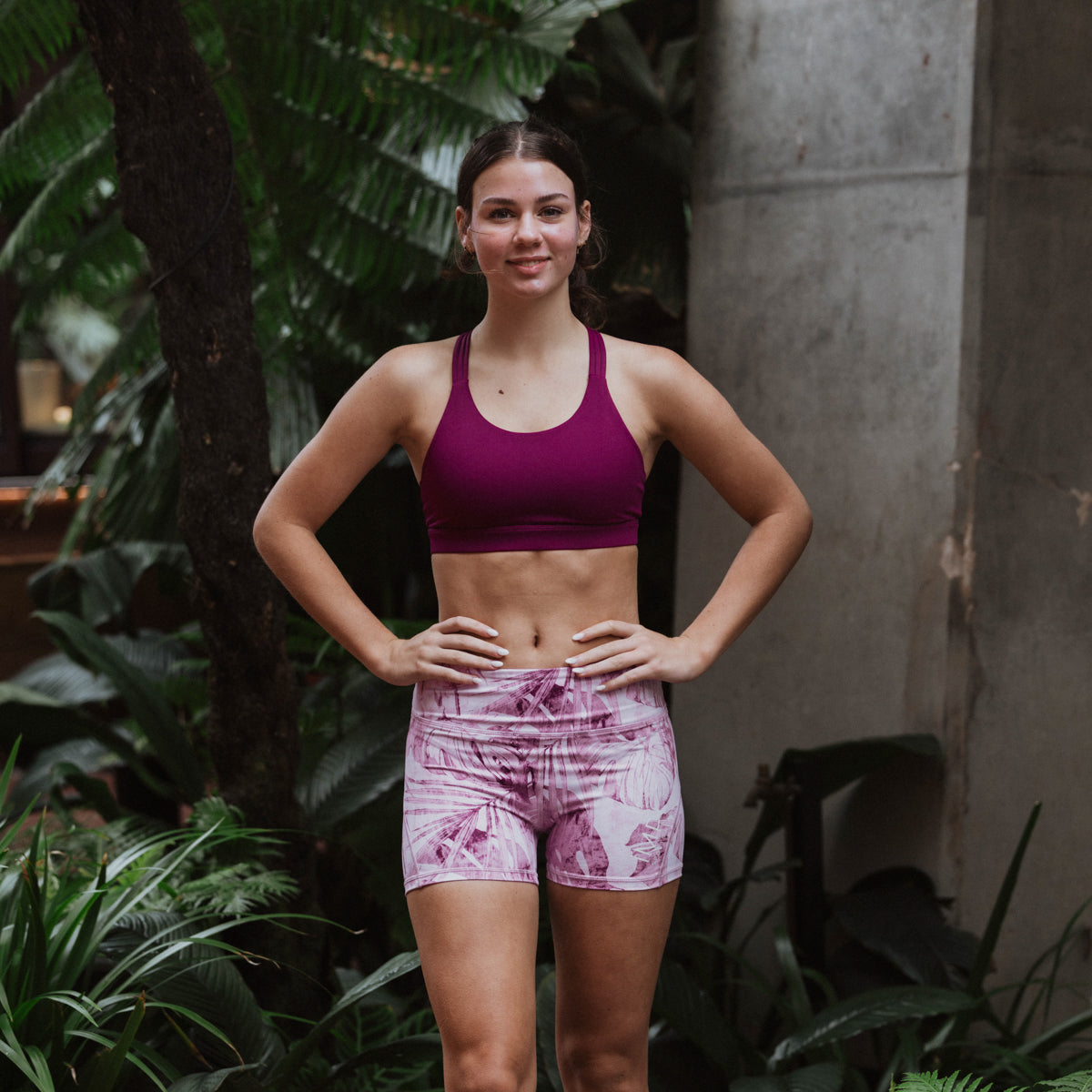 Woman in athletic wear standing outdoors with plants in the background