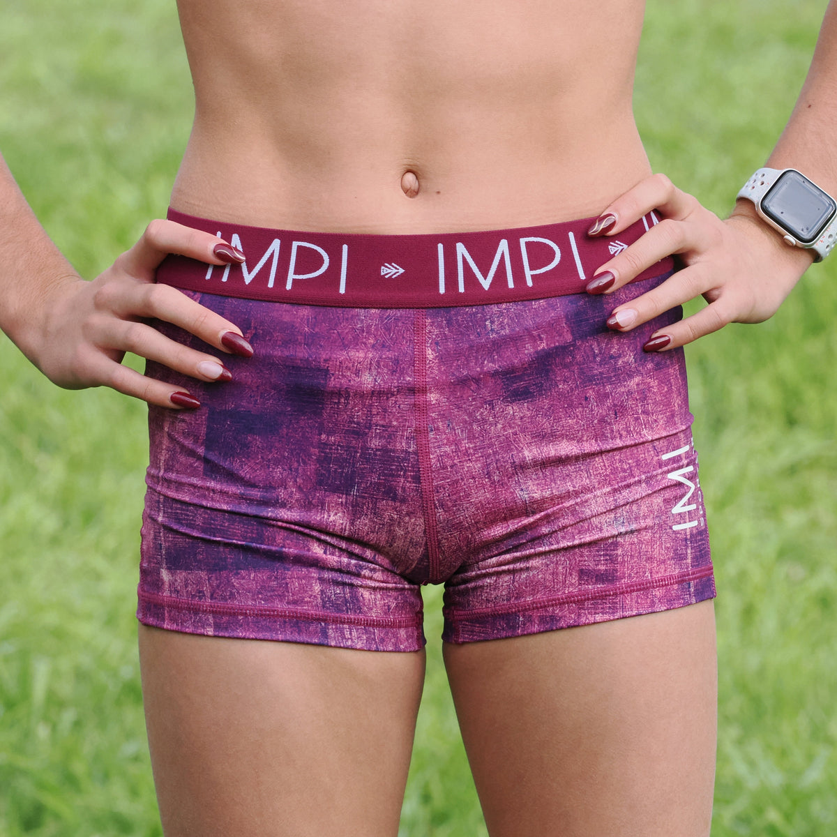 Person wearing purple athletic shorts with &#39;IMPI&#39; branding on a grassy background