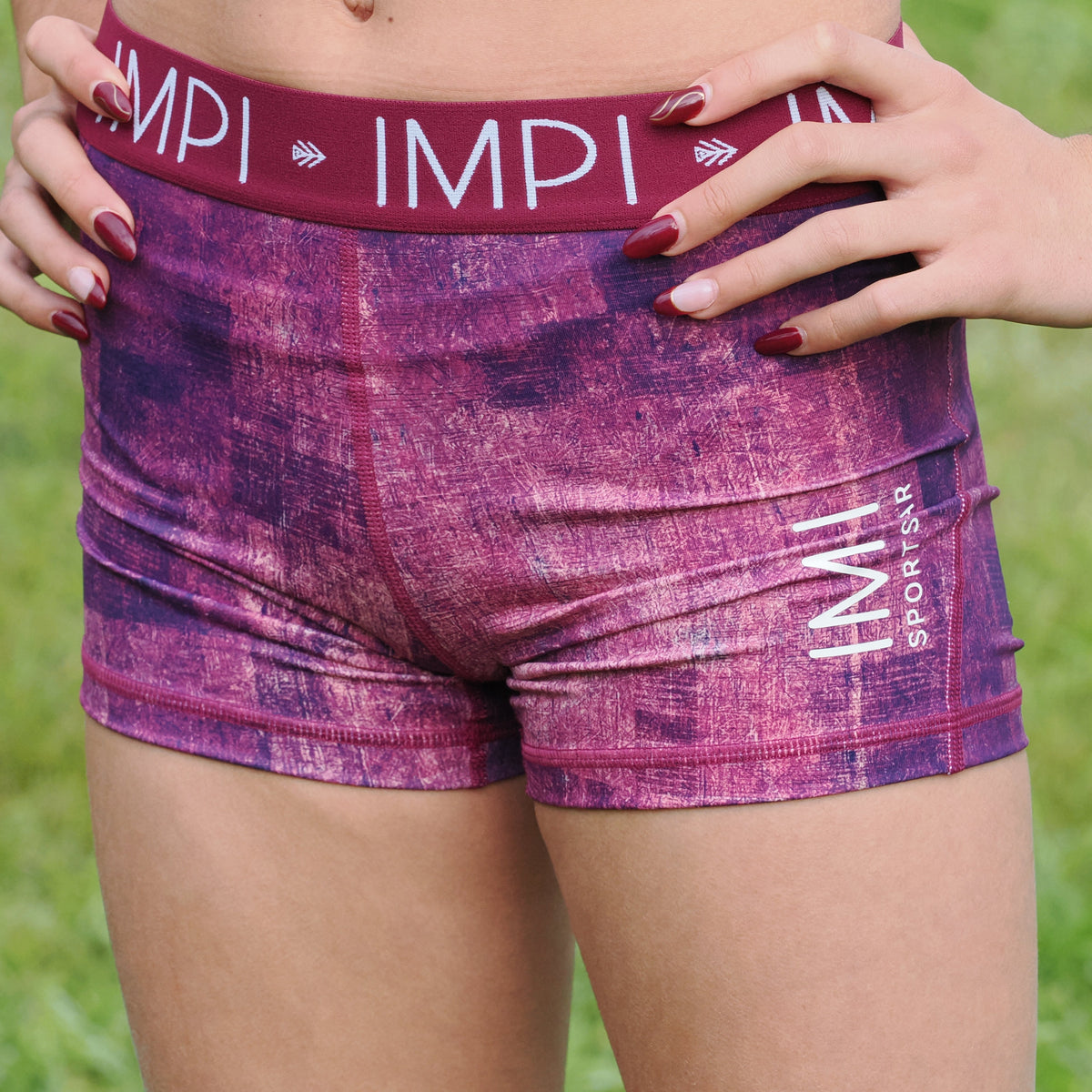 Purple athletic shorts with &#39;IMPI&#39; branding on a grassy background