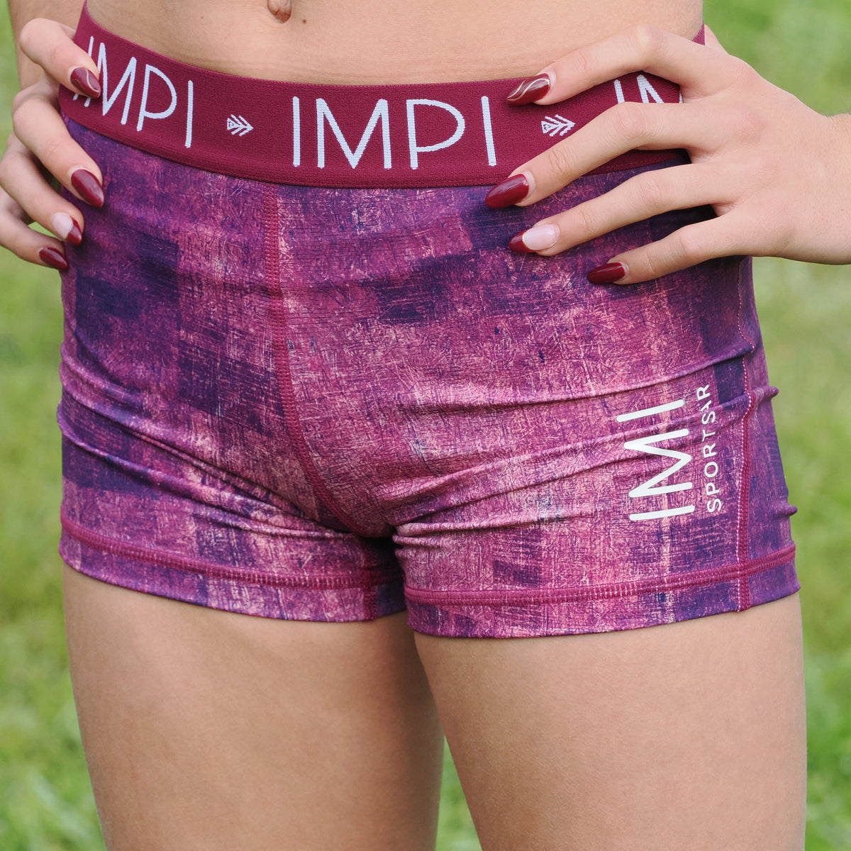 Person wearing purple athletic shorts with &#39;IMPI&#39; branding on a grassy background